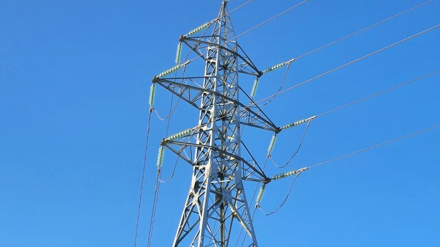low angle view of electricity transmission tower with power lines, industrial energy infrastructure set against clear blue sky