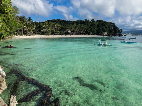 Crystal clear turquoise waters lap against the pristine white sands of Boracay's Diniwid Beach, framed by lush palm trees and local outrigger boats, offering an idyllic tropical paradise.