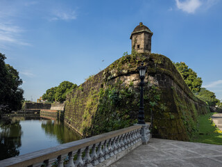 Historic Intramuros walls in Manila, Philippines, with an ancient moss-covered bastion overlooking a serene moat. A classic lamppost and stone balustrade add to the timeless charm of this iconic © BestTravelPhotos