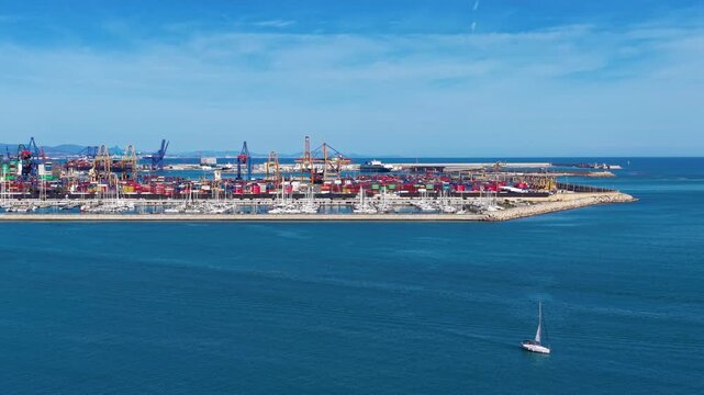 Aerial view of Spanish container port with gantry cranes, stacked containers, breakwater and marina, showing maritime logistics hub and intermodal cargo operations