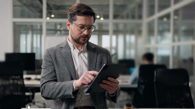 Middle-aged Caucasian business man working looking in digital tablet device wireless computer typing report adult businessman holding gadget work smiling male browsing corporate interface in office