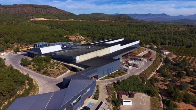Aerial view of modern waste processing plant with sorting halls, material recovery systems, loading bays and logistics yard integrated into mountainous landscape