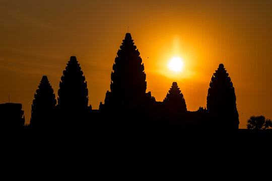 View of Angkor Wat's silhouette against the fiery sunset sky, a golden orb illuminating the ancient temple complex, Siem Reap, Siem Reap Province, Cambodia.