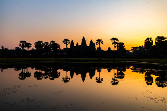 View of the majestic Angkor Wat silhouetted against a vibrant sunrise, mirrored in the tranquil waters, creating a serene and awe-inspiring scene, Siem Reap, Cambodia.