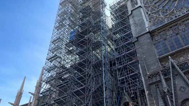 PARIS, FRANCE &ndash; 20 March, 2025: Notre Dame de Paris Cathedral part of gothic stone wall side view with scaffolding and lift moving down, restoration work after the fire, blue sky sunny day