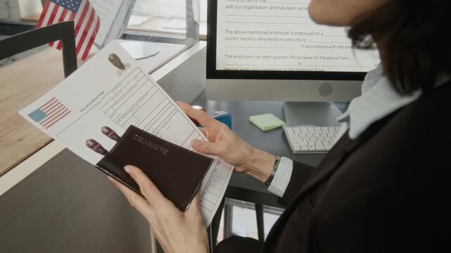 Medium panning shot of unrecognizable female USA consular officer accepting visa application from black businessman, then turning around to process and verify documents on computer