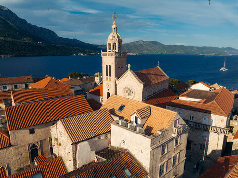 Aerial view of terracotta roofs cascading towards the azure sea, dominated by the striking bell tower of St. Mark's Cathedral, Korcula, Dubrovnik-Neretva County, Croatia.