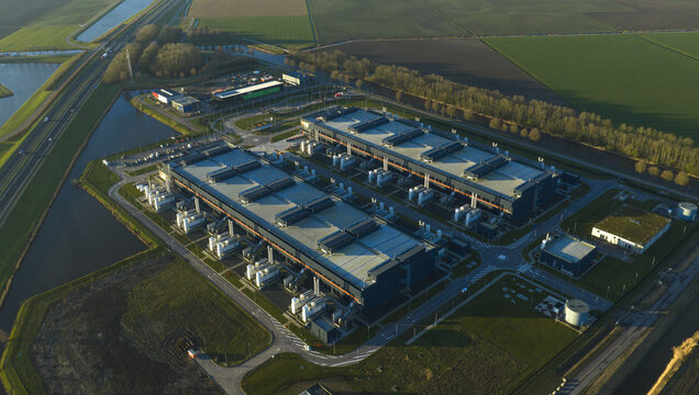 Aerial view of industrial buildings standing in stark contrast against the patchwork of green and gold fields, a modern marvel amidst rural tranquility, Middenmeer, North Holland, Netherlands.