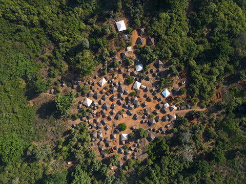 Aerial view of a traditional village with small huts and white tents nestled in a lush green forest clearing Bijagos, Guinea Bissau.
