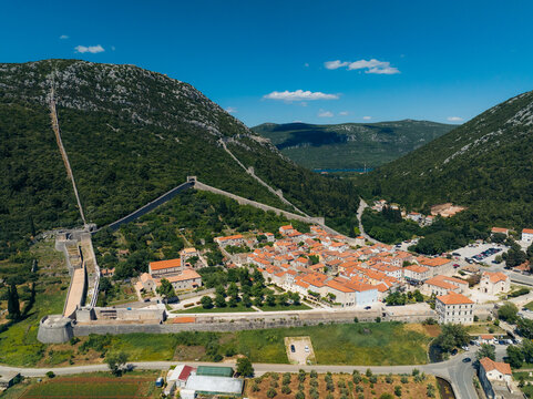 Aerial view of the ancient Walls of Ston snaking across the verdant hillsides, contrasting with the terracotta rooftops of the town below, Ston, Dubrovnik-Neretva County, Croatia.