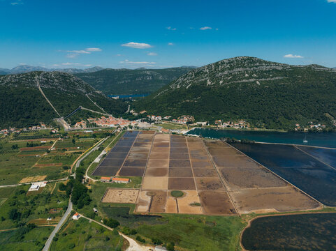 Aerial view of the geometric salt pans reflecting the azure sky, contrasting with the terracotta roofs of the town nestled between the green hills, Ston, Dubrovnik-Neretva County, Croatia.