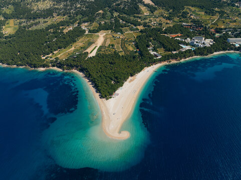 Aerial view of the golden sand beach extending into the turquoise sea, framed by lush green trees on the land, Bol, Split-Dalmatia County, Croatia.