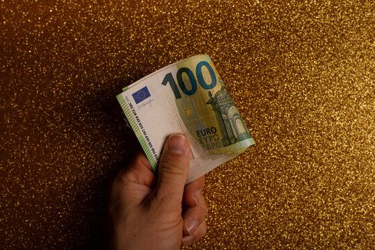 Person holding a 100 Euro banknote against a glittering golden backdrop. Concepts of wealth and fina