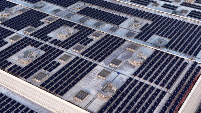 Large rooftop photovoltaic system with grid-tied solar panels, inverters, mounting racks and HVAC units on industrial building for distributed power generation