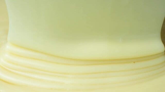 Slow motion pour of sweet condensed milk creating creamy layers.