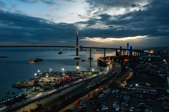 Aerial view of a long bridge extending across the water, connecting to the city's skyline, with light trails weaving through the roads below, Cebu City, Central Visayas, Philippines.