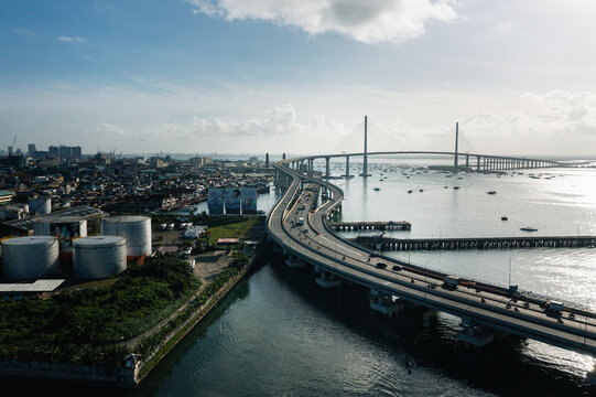 Aerial view of the Cebu-Cordova Bridge stretches across the water, linking the industrial port area with the cityscape under a bright sky, Cebu City, Central Visayas, Philippines.
