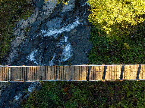 Aerial view of a wooden bridge stretching over a rocky riverbed where water flows, flanked by lush green vegetation, Foz d'Egua, Coimbra, Portugal.