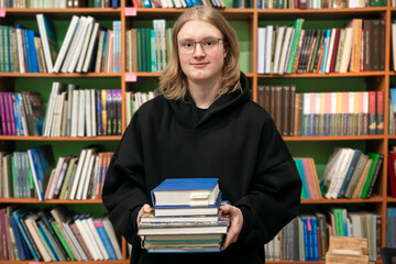 Young smiling man in a library holding stack of books