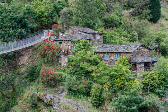 Aerial view of stone houses nestled amongst vibrant greenery, connected by a modern bridge, creating a striking contrast between old and new, Foz d'Egua, Arganil, Portugal.