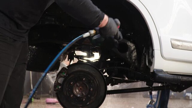 Washing the rear suspension, bottom of an car with a high-pressure water jet at a self-service car wash. Washing the suspension of the car from reagents and dirt using high water pressure. Car care.