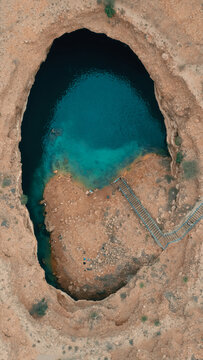 Aerial view of Sink Hole with turquoise water and a staircase leading down into the rocky crater Dhofar Governorate, Oman.