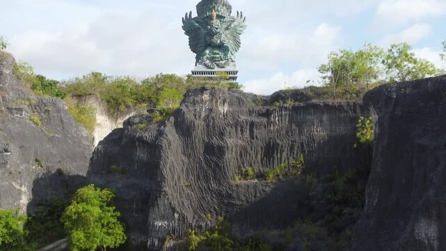 Cinematic aerial drone lifting off and ascending to reveal the monumental Garuda Wisnu Kencana statue in Bali, Indonesia.