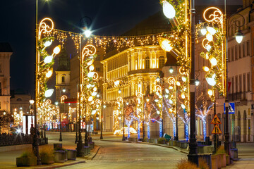 Christmas lights and illuminated trees decorate a historic street in Warsaw, Poland, at night during winter season.