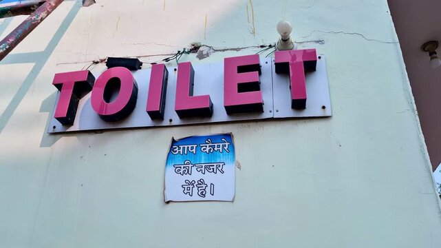 Public toilet signboard, with Hindi notice saying �Aap camera ki nazar mein hain� (You are under CCTV surveillance) on the wall below the TOILET sign.