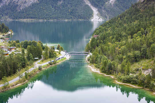 Aerial view of the bridge spanning the serene turquoise waters, nestled between verdant forests under the crisp mountain air, Plansee, Tyrol, Austria.