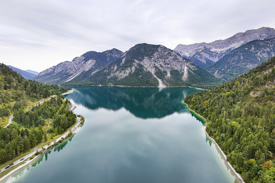 Aerial view of the serene Plansee lake mirroring the majestic Alps, nestled between verdant forests under a soft sky, Plansee, Tyrol, Austria.