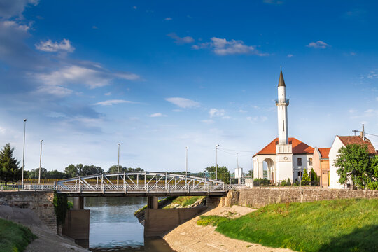Panorama of the Atik Savska Dzamija mosque rising above the Brka river in Brcko District, Bosnia and Herzegovina, with bridge, calm water and clear blue sky in a bright urban riverside setting.