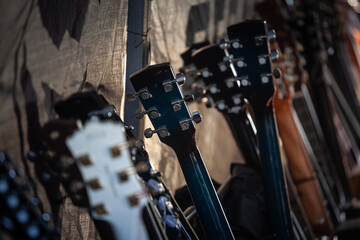 Fototapeta premium Close-up of a row of electric guitar headstocks lined up against a dark textured backdrop, highlighting tuning pegs, instrument variety and the process of choosing the right guitar in a music store.
