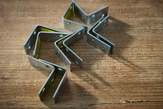 Create shapes with metal brackets on wooden surface in a workshop setting during the day