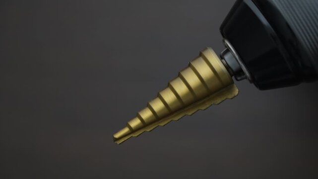 Conical step drill clamped in electric screwdriver rotates, close up. Step conical drill bit for drilling holes with different diameters on the wooden background. Hss step drill bit