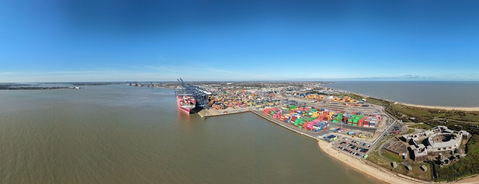 Aerial view of the bustling Port of Felixstowe, where a colossal container ship meets a kaleidoscope of multicolored containers under a vast, clear sky, Felixstowe, United Kingdom.