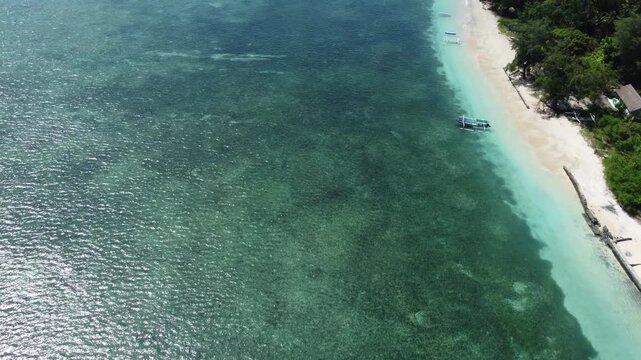 Cinematic aerial drone flying forward in slanted top down view above clear shallow water and coastline of Gili Air, Indonesia.