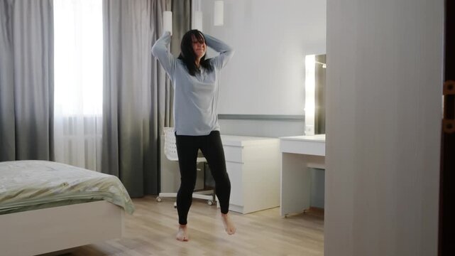 White woman dancing freestyle in bedroom with bare feet, energetic footwork, flowing shirt, window light, music driven gestures, expressive rehearsal, joyful cardio, body positive movement