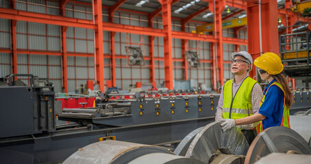Fototapeta premium Exhausted senior factory worker wiping sweat while working on production line with colleague. Industrial teamwork, manufacturing effort, and workplace fatigue concept.