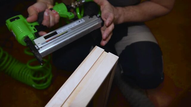 Craftsman in a carpentry workshop hammers nails with a pneumatic hammer. Making a wooden box. A close-up pneumatic nail gun putting nails in boards.