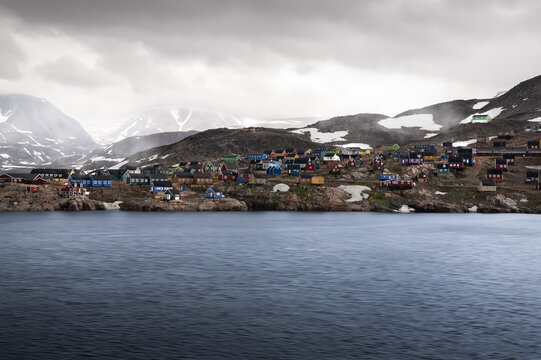 View of colorful wooden houses scattered across a rocky hillside overlooking the water under a cloudy sky in Ittoqqortoormiit, Sermersooq Municipality, Greenland.