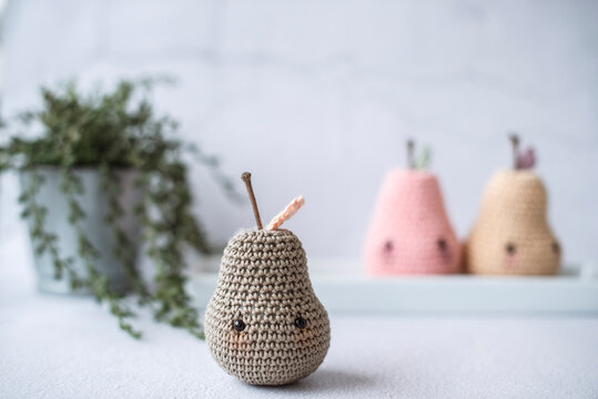 Close-up of three homemade assorted anthropomorphic crochet pear toys (Amigurumi) on a table with a houseplant