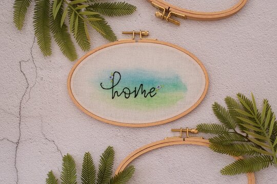 Overhead view of an embroidery hoop with the word home on a  table with fern branches