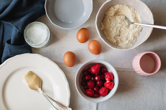 Overhead view of assorted Baking ingredients for making a cake including eggs, strawberries, cherries, coconut oil and gluten free almond and coconut flour