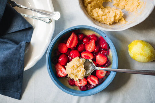 Overhead view of gluten-free dough being added to fresh strawberries and cherries in a silicone baking mould