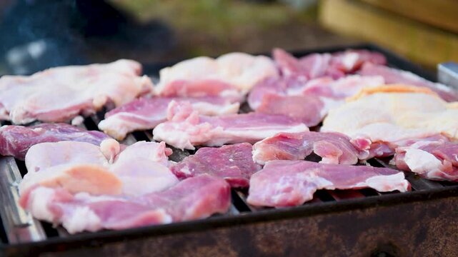 Grill full of chicken and pork meat, still red and raw close up, grill master hand move pieces and add new one