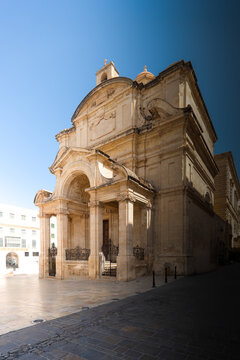 View of the historic Church of Our Lady of Victories with its ornate limestone facade and classical columns under a clear blue sky in Valletta, Malta.