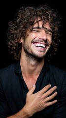 Obraz premium Young caucasian male with curly hair laughing against black background