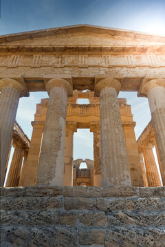 View of the ancient Doric columns of the Valley of the Temples under a bright blue sky in Agrigento, Sicily, Italy.