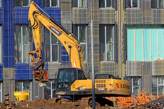 The excavator uses a bucket on metal chains to carry the metal mounting structure. 